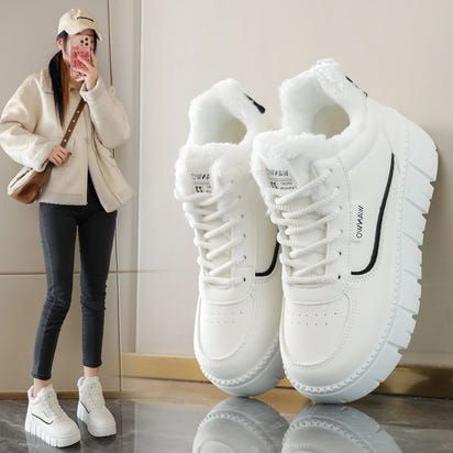 White sneakers with black accents on a reflective surface, next to a person wearing similar shoes indoors.